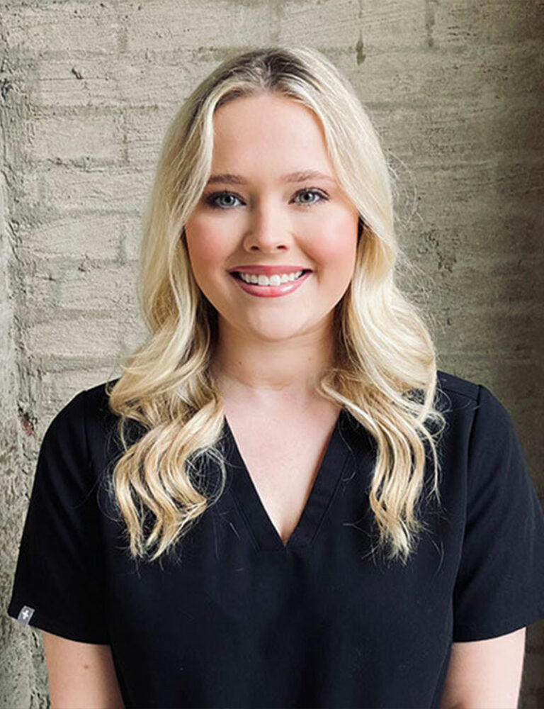 Headshot of Peyton wearing a black scrub against a wall.