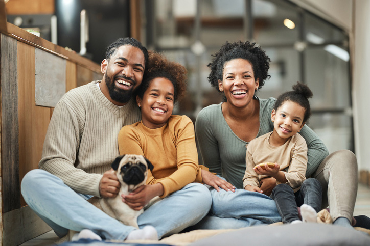 family photo of parents and two kids sitting on the parents laps with a dog