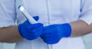 A dental assistant wearing blue medical gloves holds an intraoral camera