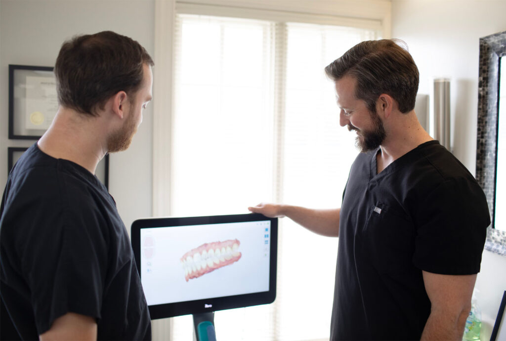 Dr. Hall and Dr. Alison examine a screen displaying a 3D dental model in a clinic environment, emphasizing the integration of modern technology in dentistry.