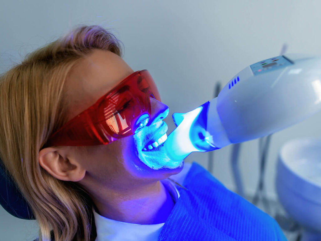 female patient wearing protective glasses while having her teeth whitened with LED light
