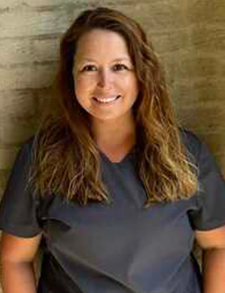 Headshot photo of Nikki wearing a gray scrub against a wall.